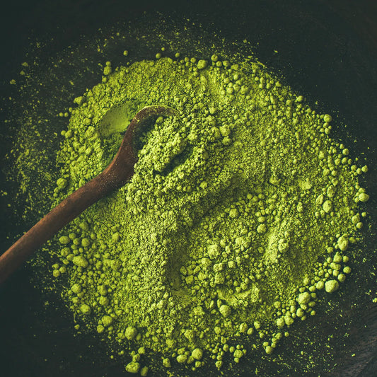 Colorful green tea powder sprinkled on a wooden spoon placed on a dark table.