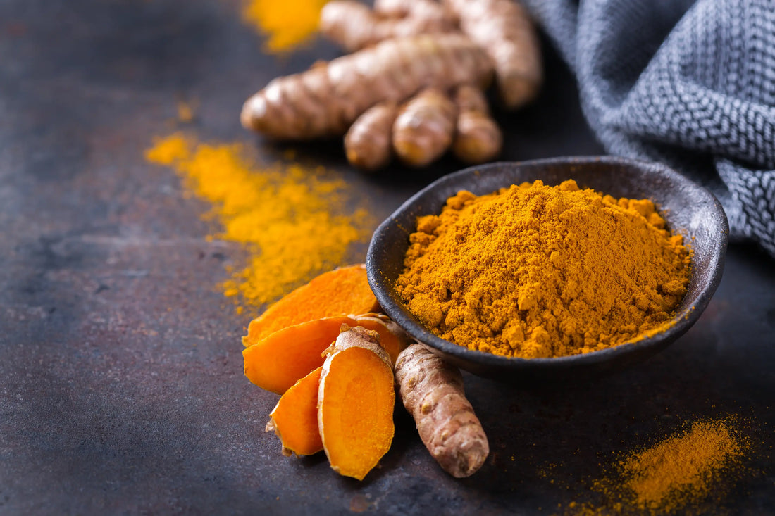 Fresh turmeric roots and ground turmeric in a bowl on a slate table.