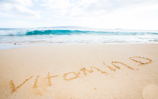 The word Vitamin D written in the sand on a beach with waves in the background